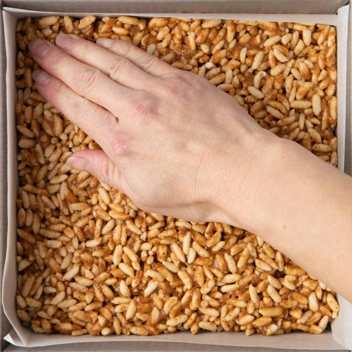 Hand pressing mixture down in one corner, showing most of it already pressed down.