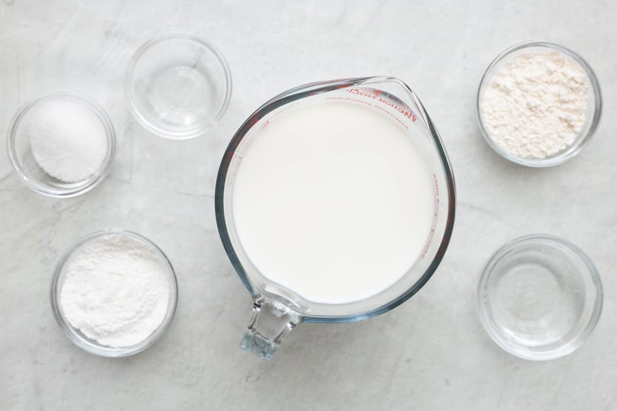 Ingredients for recipe in individual bowls: whole milk, vinegar, flour, cornstarch, sugar, and orange blossom water.