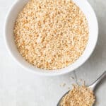 Small serving bowl of toasted seasame seeds with a spoon next to it overflowing with more seeds.