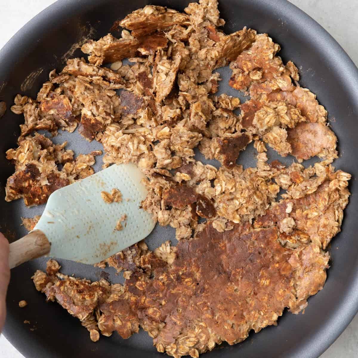 Spatula pushing the partially browned oat mixture around skillet.