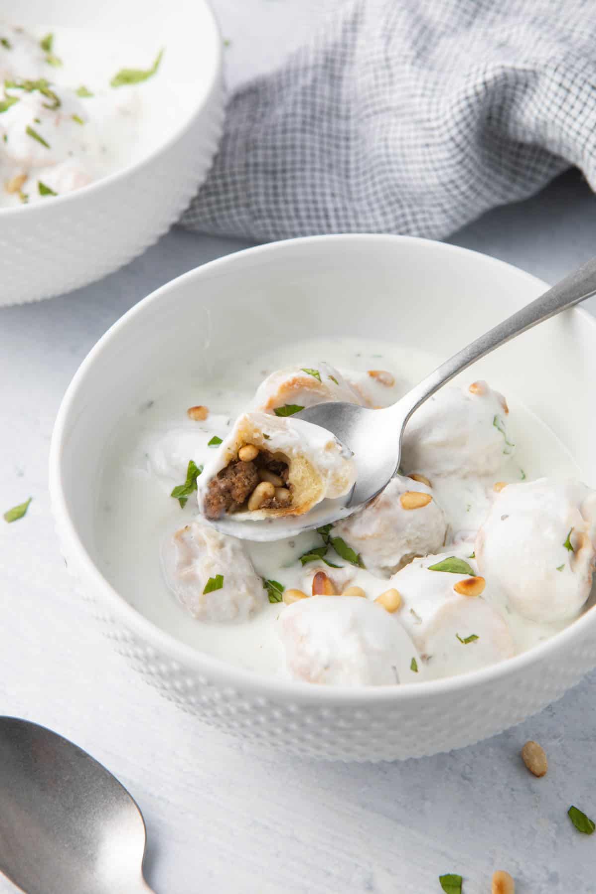 Spoon lifting up a dumpling from a bowl of Shish Barak that is cut open to show beef and nut mixture inside.