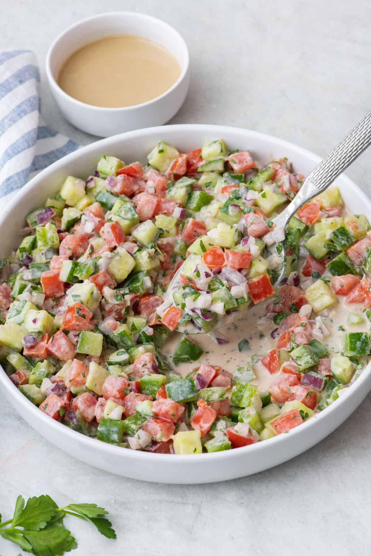Tahini salad full of fresh chopped vegetables in a bowl with a spoon scooping some up.
