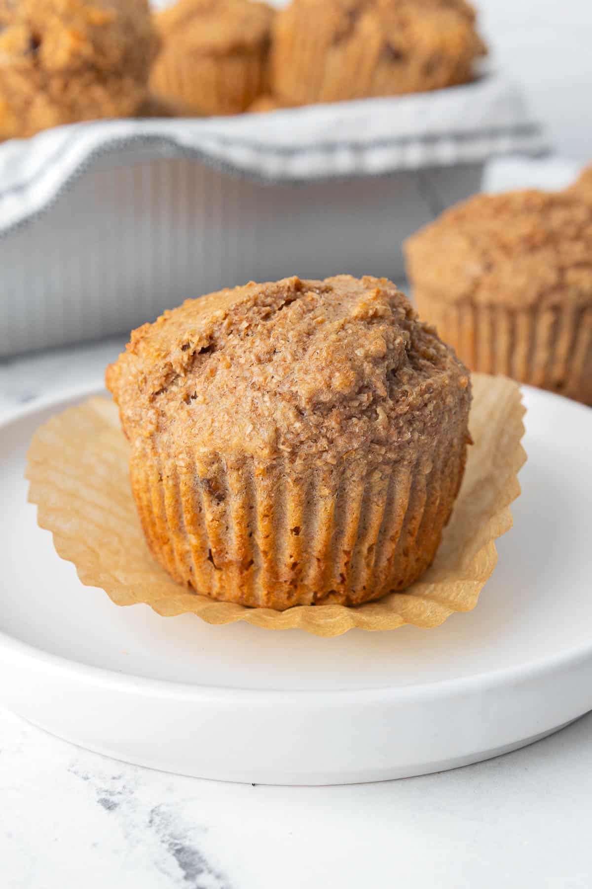 Bran muffin on a plate with the paper peeled away.