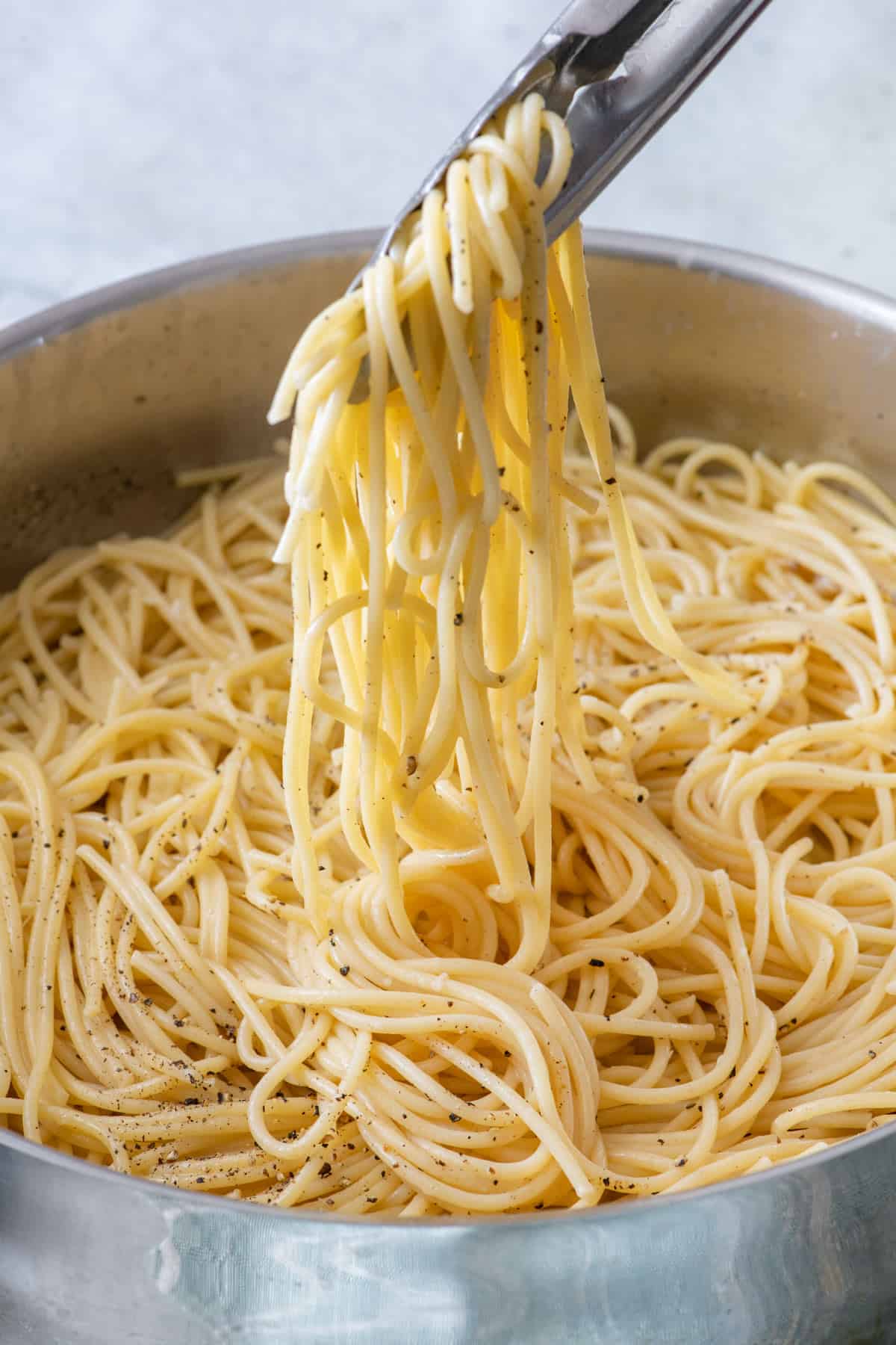 Tongs lifting up Cacio e pepe from pot.