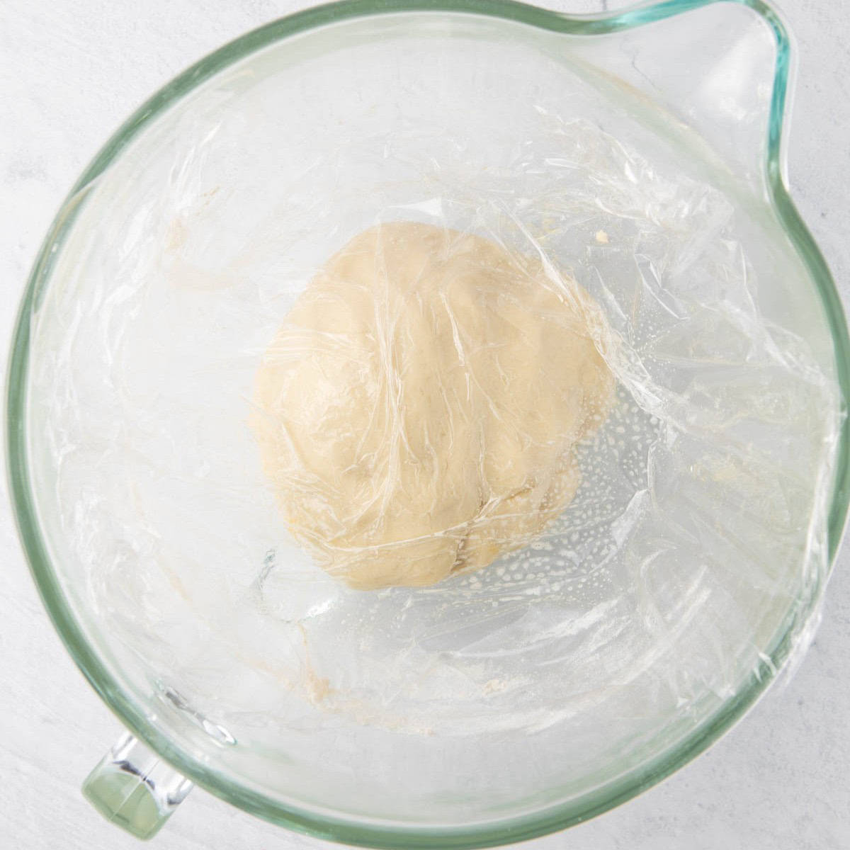 Oiled plastic wrap set on top of dough ball in stand mixer bowl.