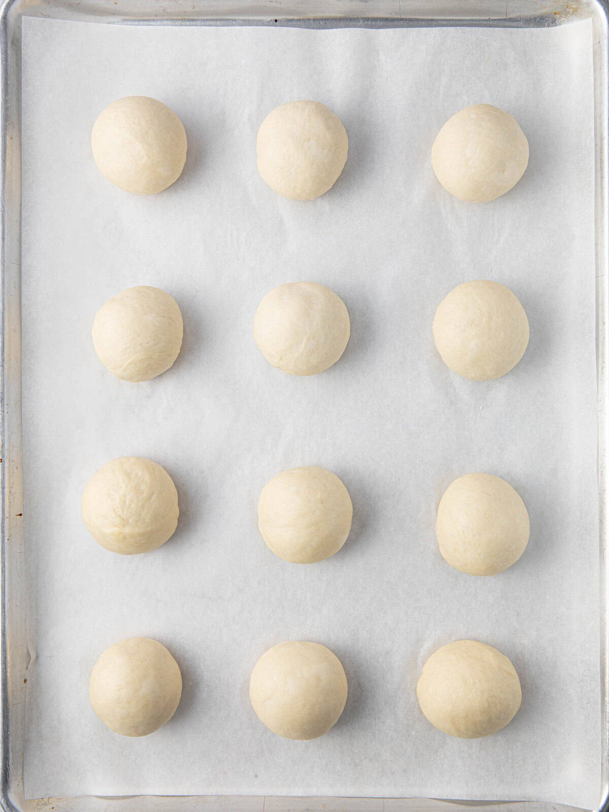 12 dough balls on a baking sheet lined with parchment paper before resting.