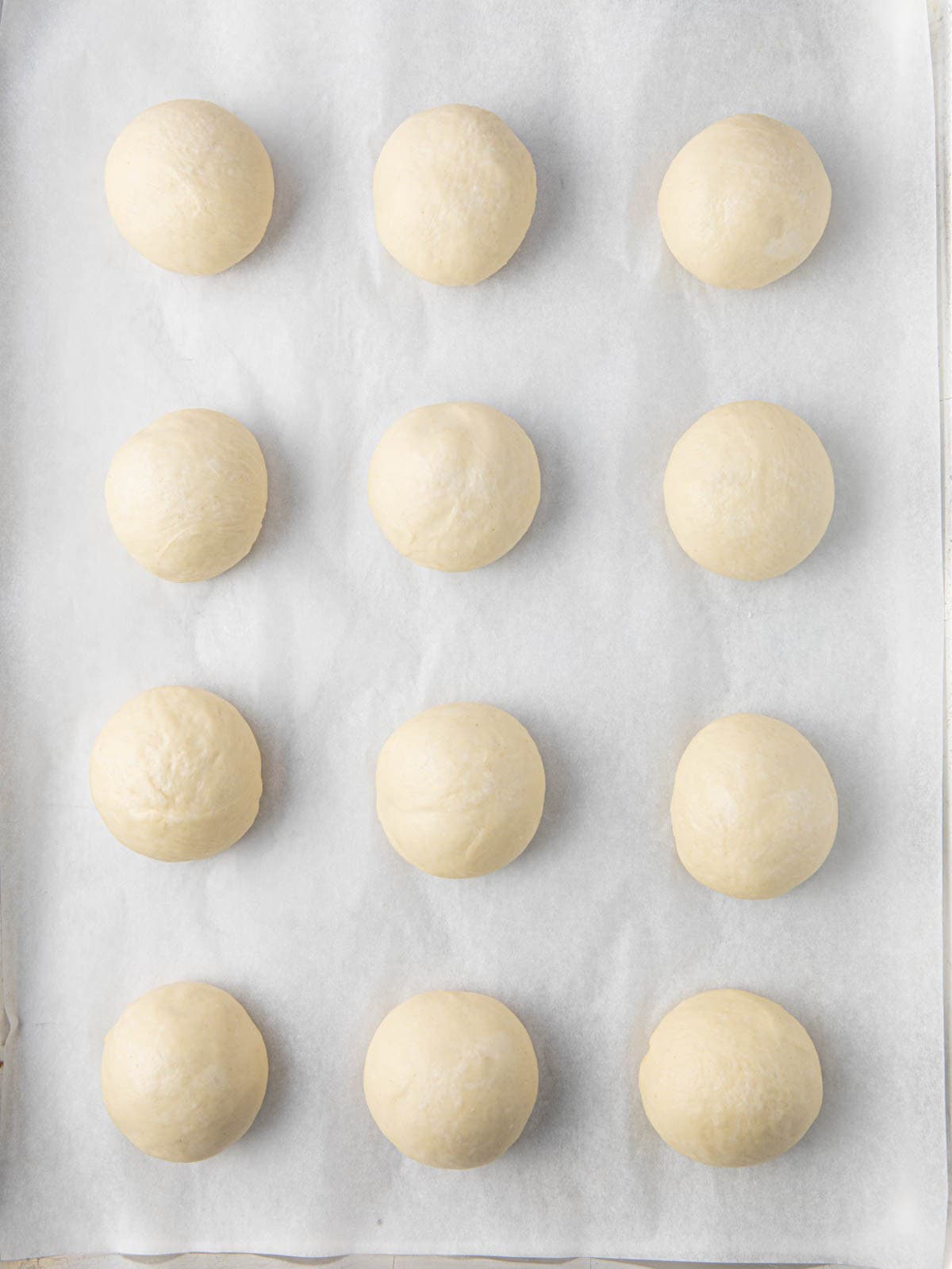 12 dough balls on baking sheet after resting for 10 minutes showing them slightly bigger.