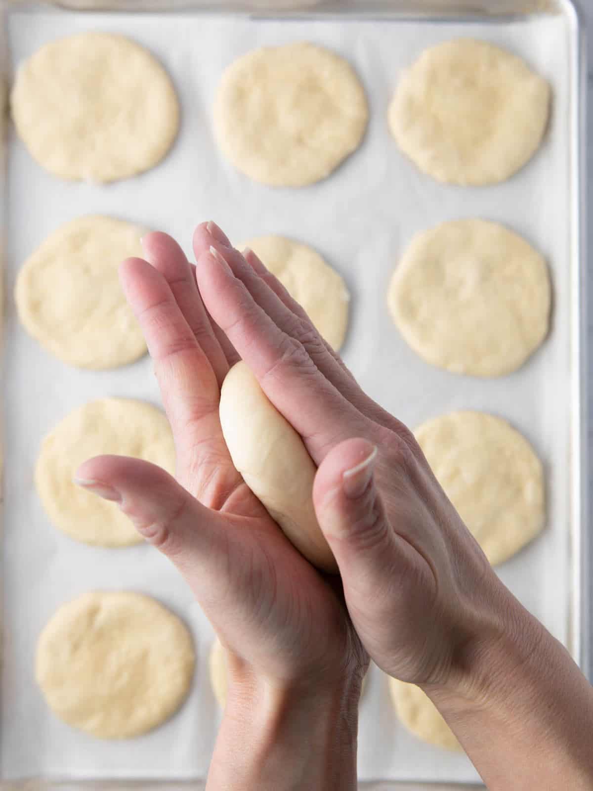 12 flatbreads on baking sheet with hand pressing last one of them in flat disc.