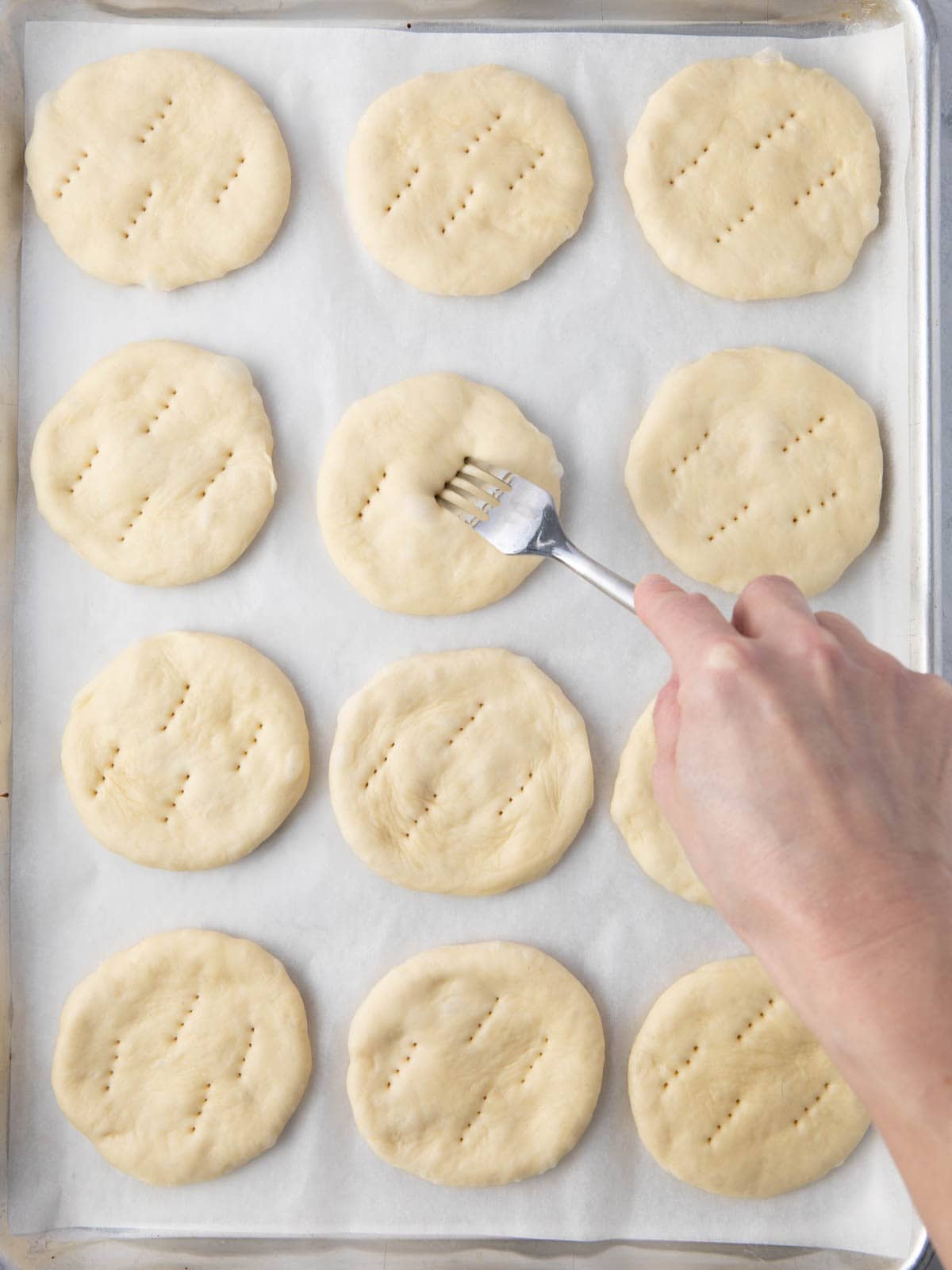 12 flatbreads on baking sheet all poked with fork and fork poking last one of them.
