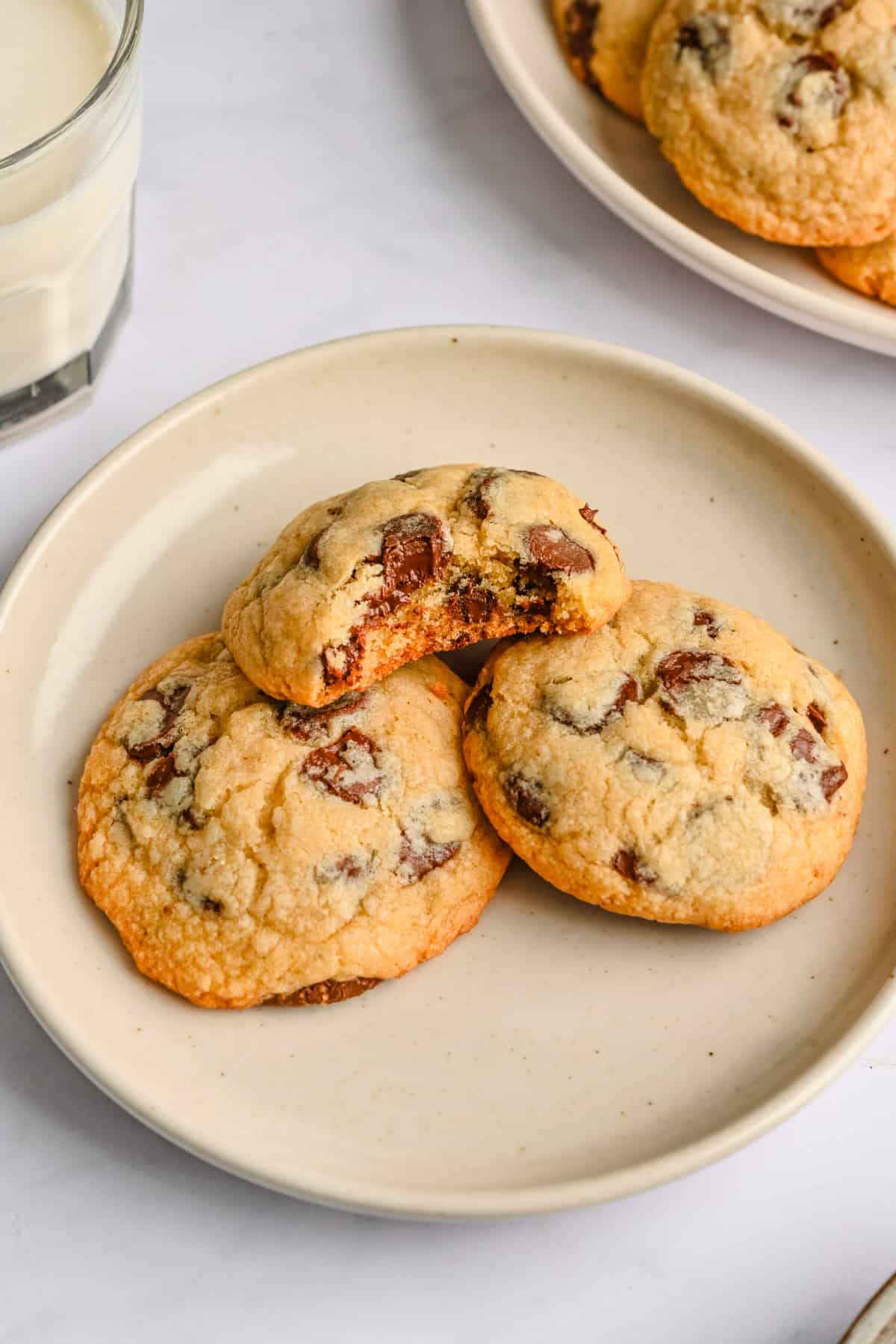 Chocolate chip cookies on a wire rack stacked over each other with a small dish of chocolate chips nearby.