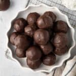 Chocolate coconut balls on a decorative plate with extra shredded coconut and melted chocolate nearby.