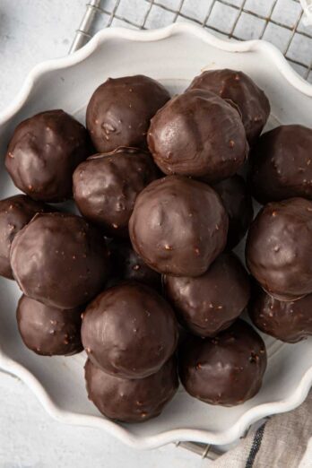 Chocolate coconut balls on a decorative plate with extra shredded coconut and melted chocolate nearby.