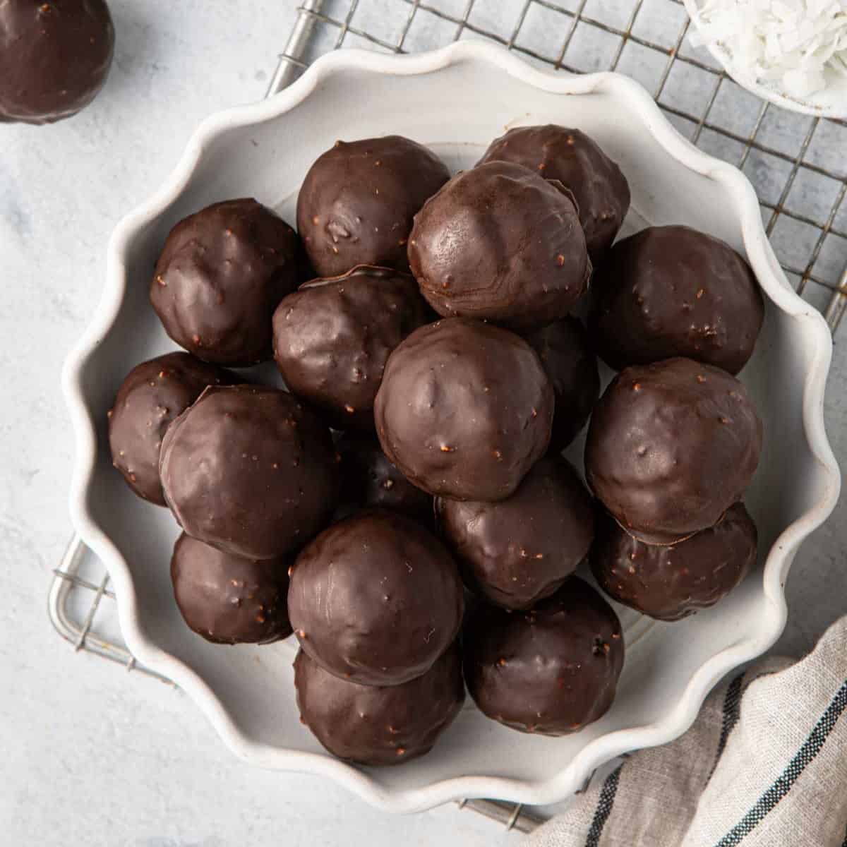 Chocolate coconut balls on a decorative plate with extra shredded coconut and melted chocolate nearby.
