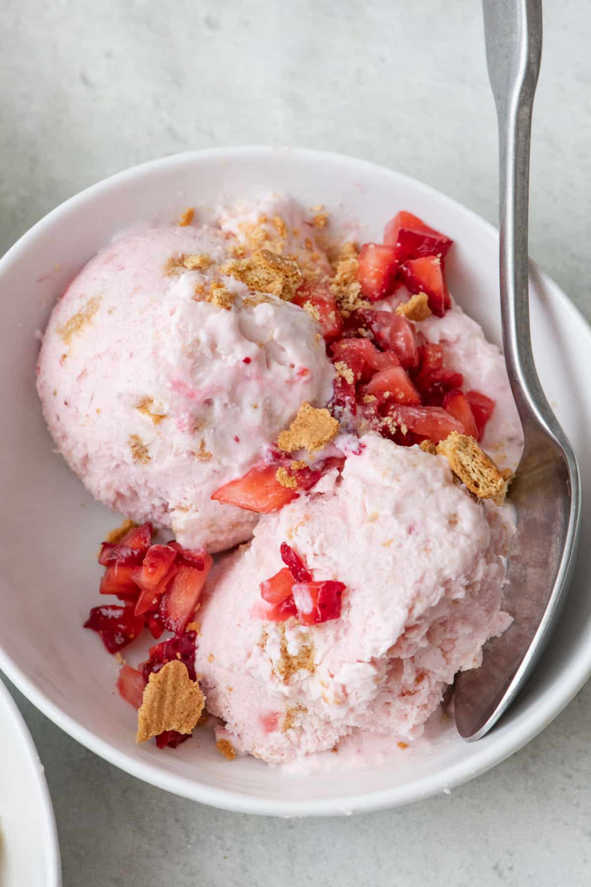 Strawberry cheesecake cottage cheese ice cream in a bowl with extra fruit and graham crackers on top.