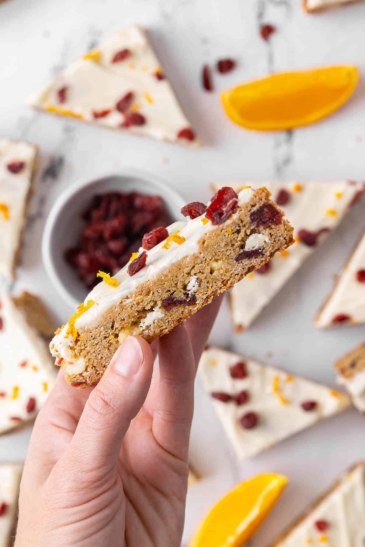 Hand holding a cranberry bliss bar up close above more bars.