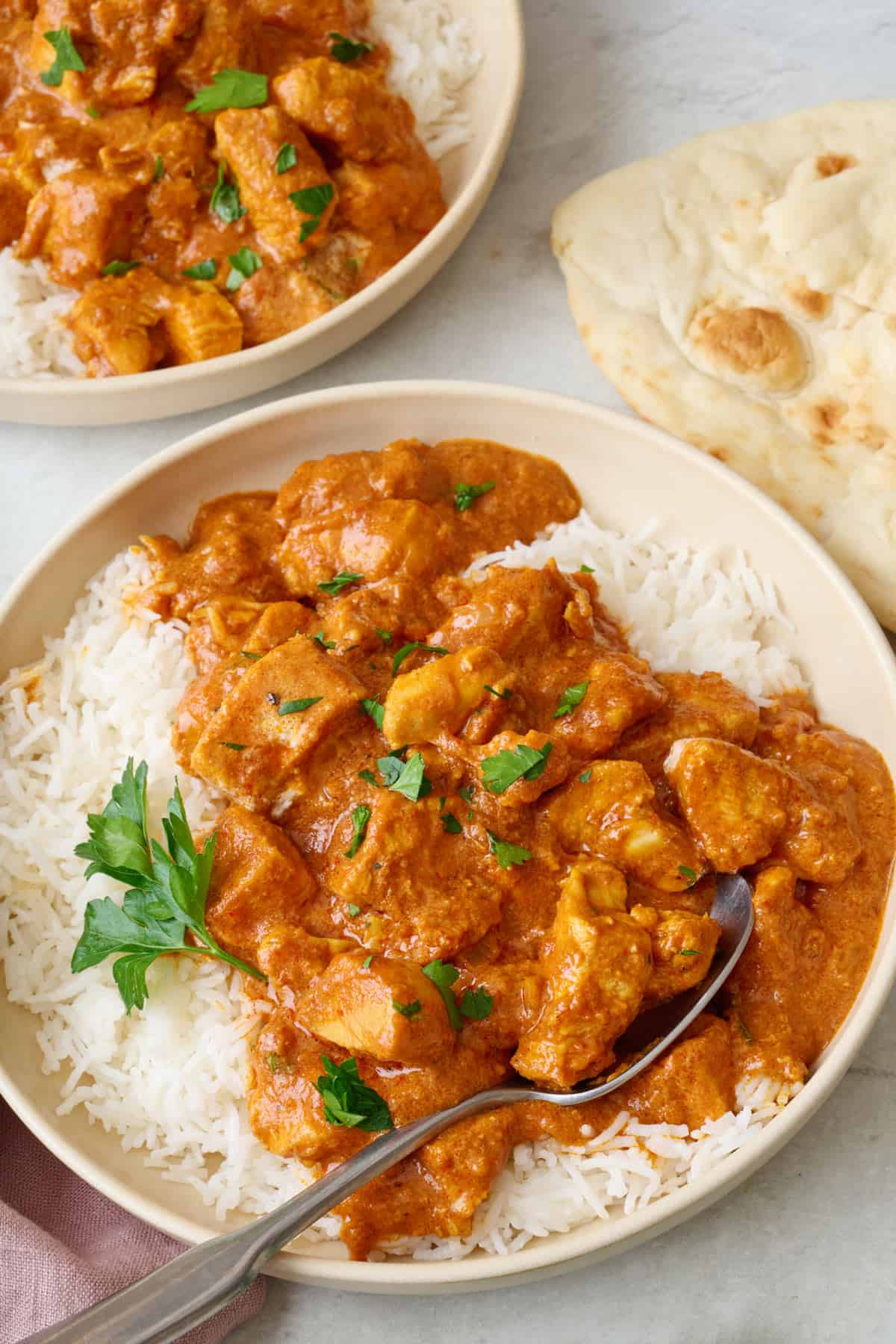 Close up of the final dish for the easy butter chicken plates with rice and cilantro and a spoon dipped in.