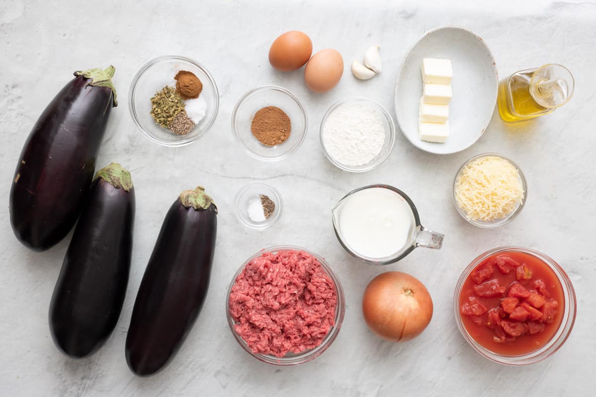 Ingredients to make recipe: egg plants, herbs and spices, ground beef, onion, tomatoes, eggs, flour, garlic, butter, mikl, parmesan cheese, and oil.