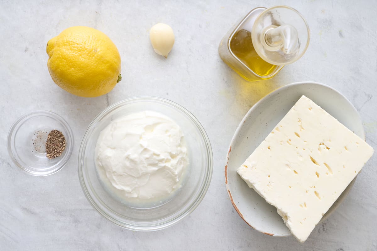 Ingredients for recipe: block of feta cheese, greek yogurt, pepper, lemon, garlic, and olive oil.