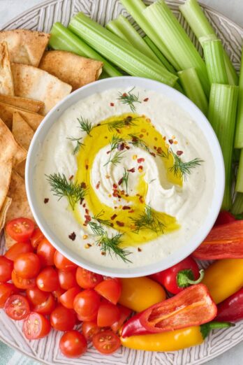 Platter of pita chips and fresh veggies with bowl of feta dip in center.