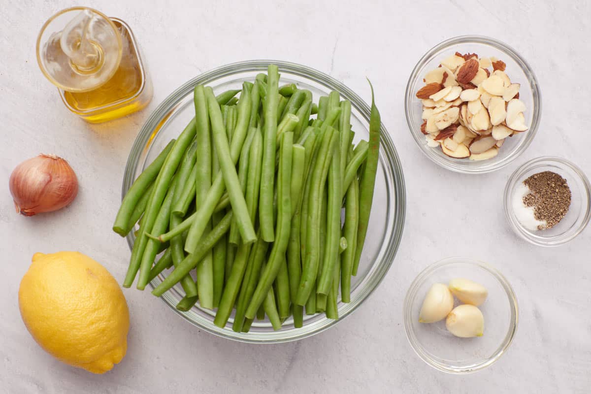 Plate of green beans after being trimmed. Next to the plate is parmesan cheese, lemon slices and garlic