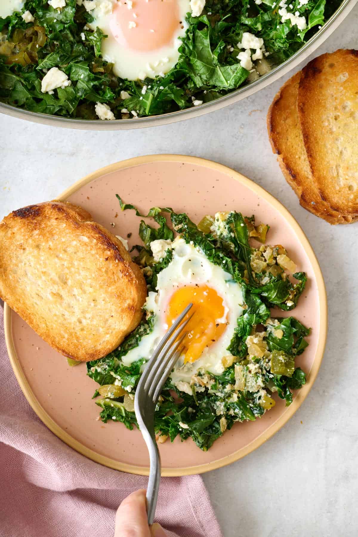 Cutting into an egg on a plate of green shakshuka