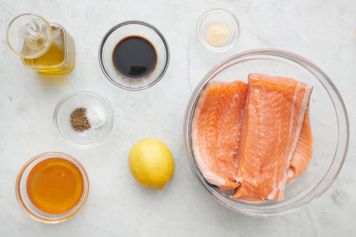 Ingredients to make the recipe including salmon, lemon, honey, coconut oil, along with kale, quinoa, cherries and feta cheese for the salad