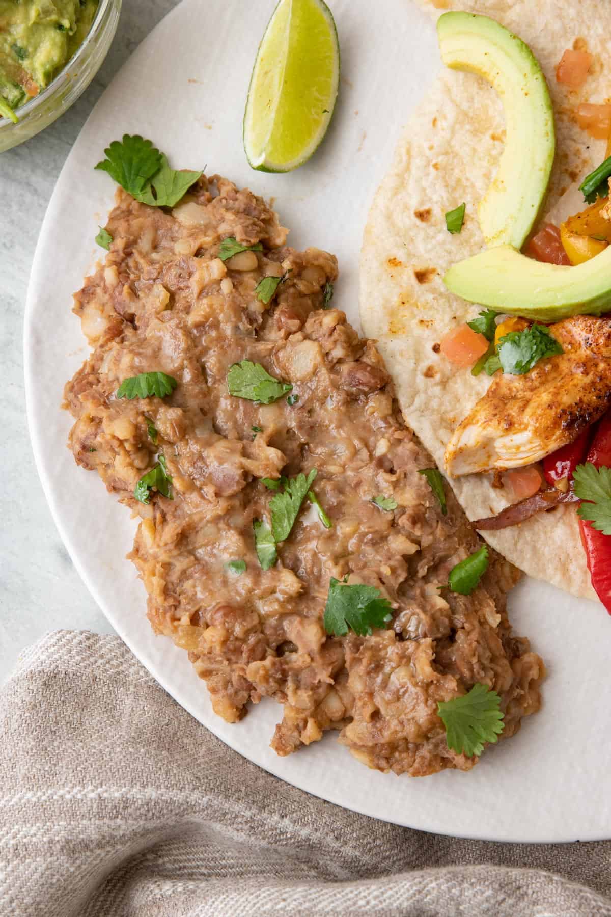 Serving of beans on a round plate next to chicken fajitas.