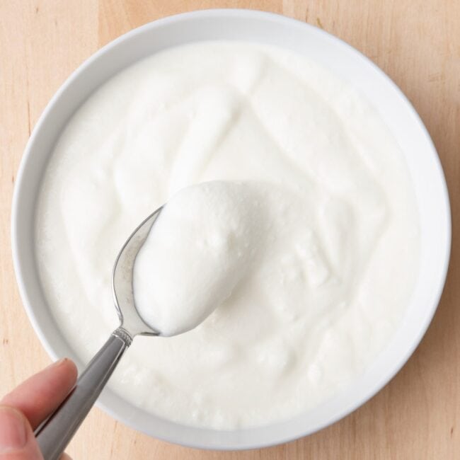 Yogurt in small bowl with spoon lifting up some yogurt.