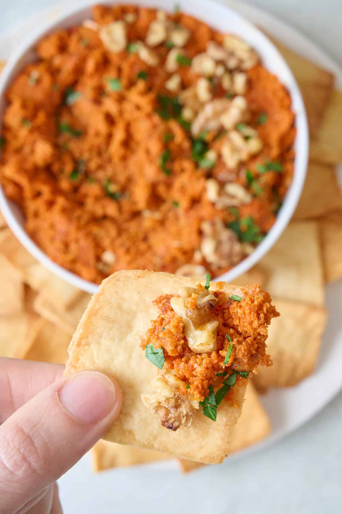 Close up of muhammara dip with a pita chip being dipped in