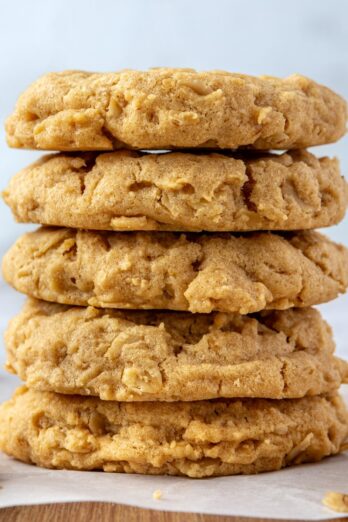 Peanut butter oatmeal cookies on parchment paper with a small jar of peanut butter and a spoon nearby.