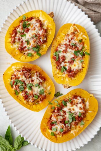 Four spaghetti squash lasagna halves on a large decorative platter topped with melty cheese.