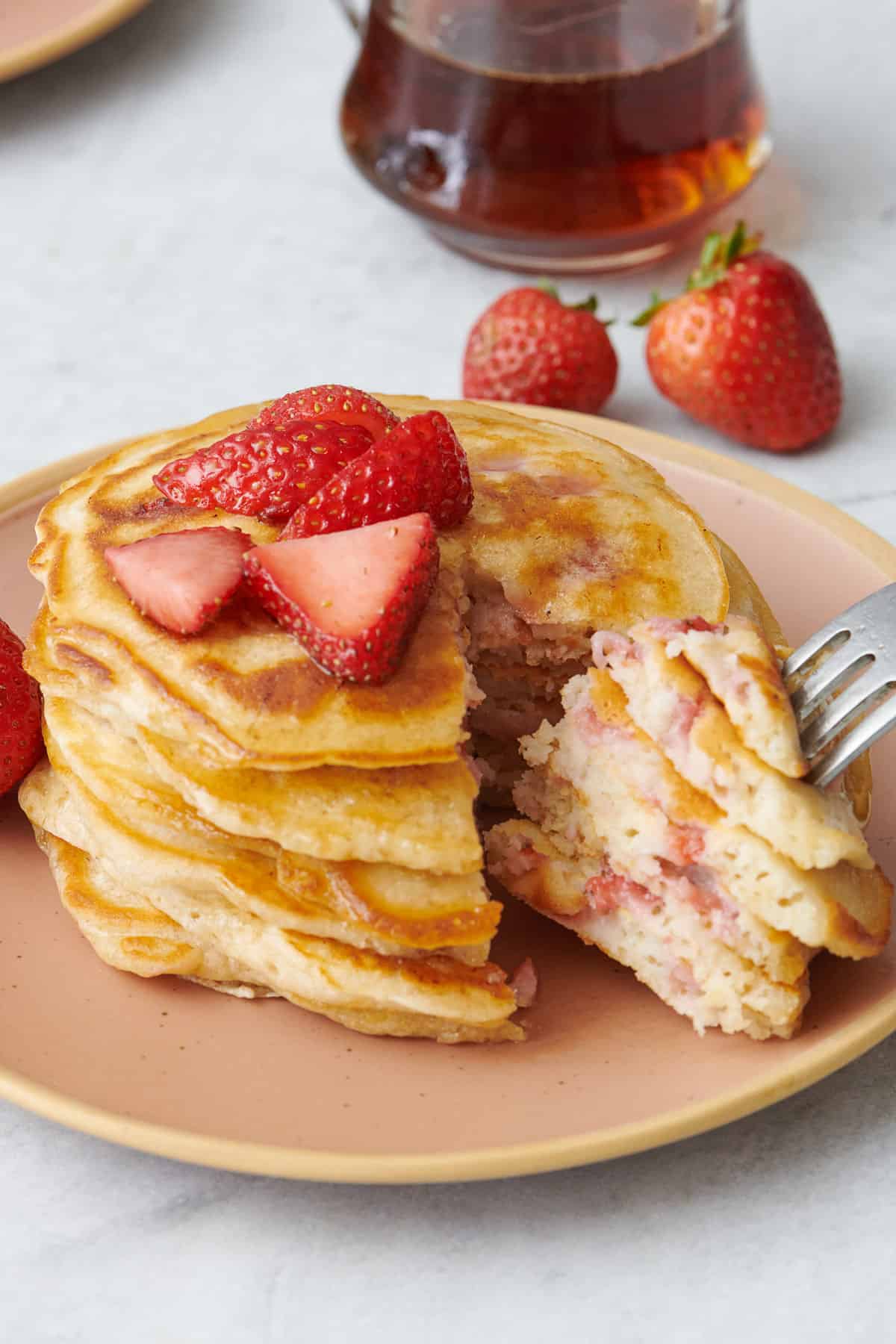 Fork piercing a bite from a stack of strawberry pancakes.