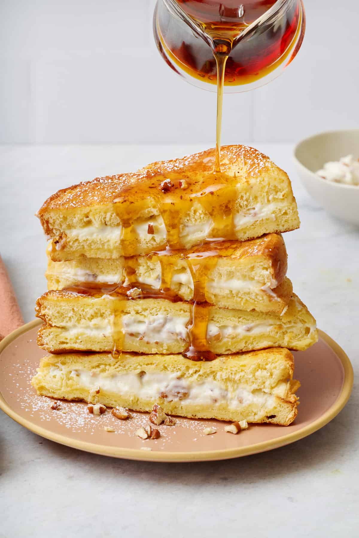 Final plating of the stuffed french toast with two stacked on top of each other, topped with bananas and maple syrup getting drizzled on top