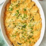 Zucchini casserole baked in an oval dish with a golden brown breadcrumb topping, garnished with fresh chopped parsley.