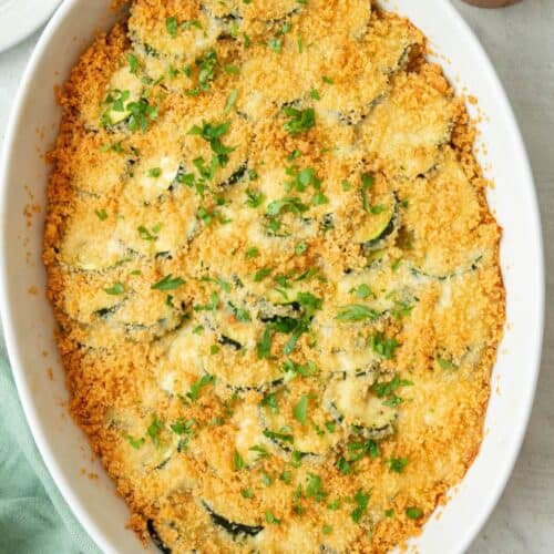 Zucchini casserole baked in an oval dish with a golden brown breadcrumb topping, garnished with fresh chopped parsley.