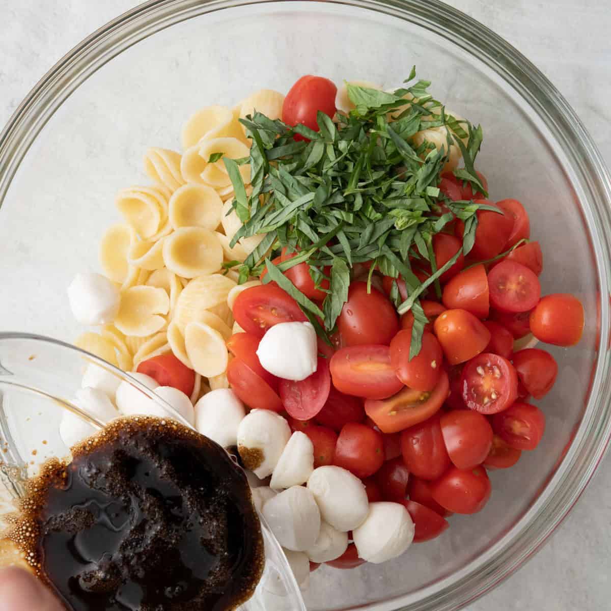 Dressing being poured over pasta.
