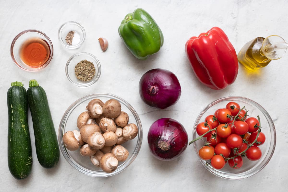 Ingredients for recipes: zucchini, mushrooms, red and green bell peppers, red onions, cherry tomatoes, vinegar, seasonings, garlic, and oil.