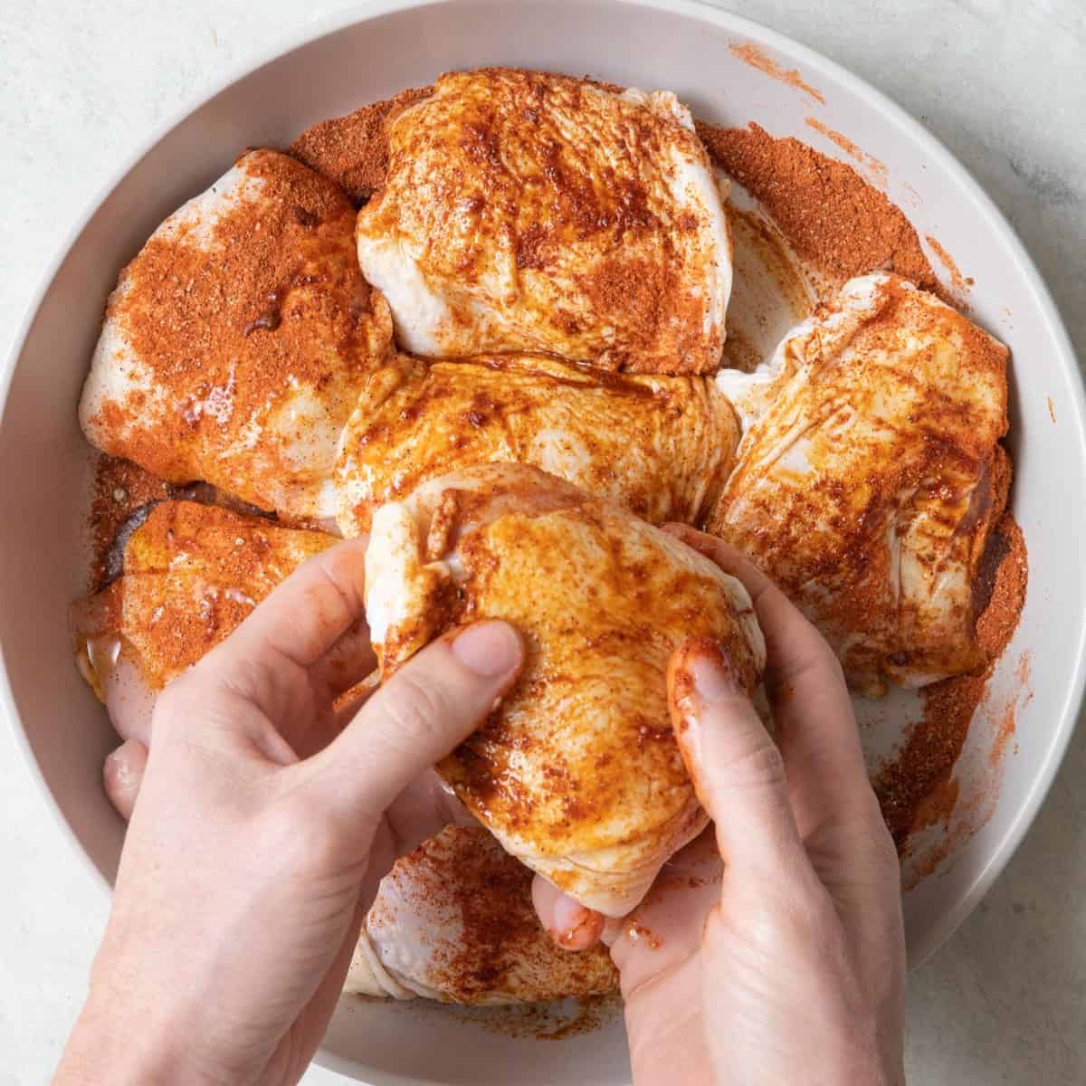 Hands rubbing the oil and seasoning over the thighs.
