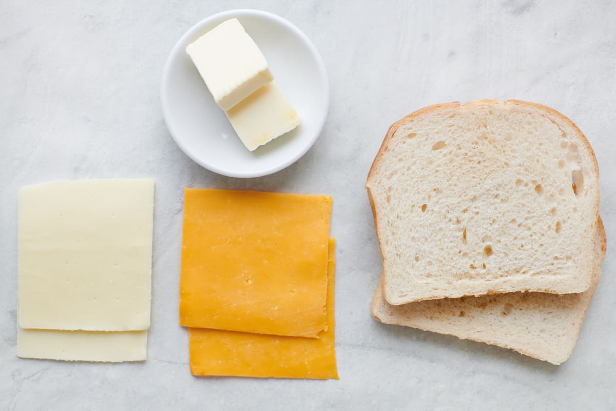 Ingredients for recipe: 2 slices of mozzarella, 2 slices of cheddar, butter, and sliced bread.