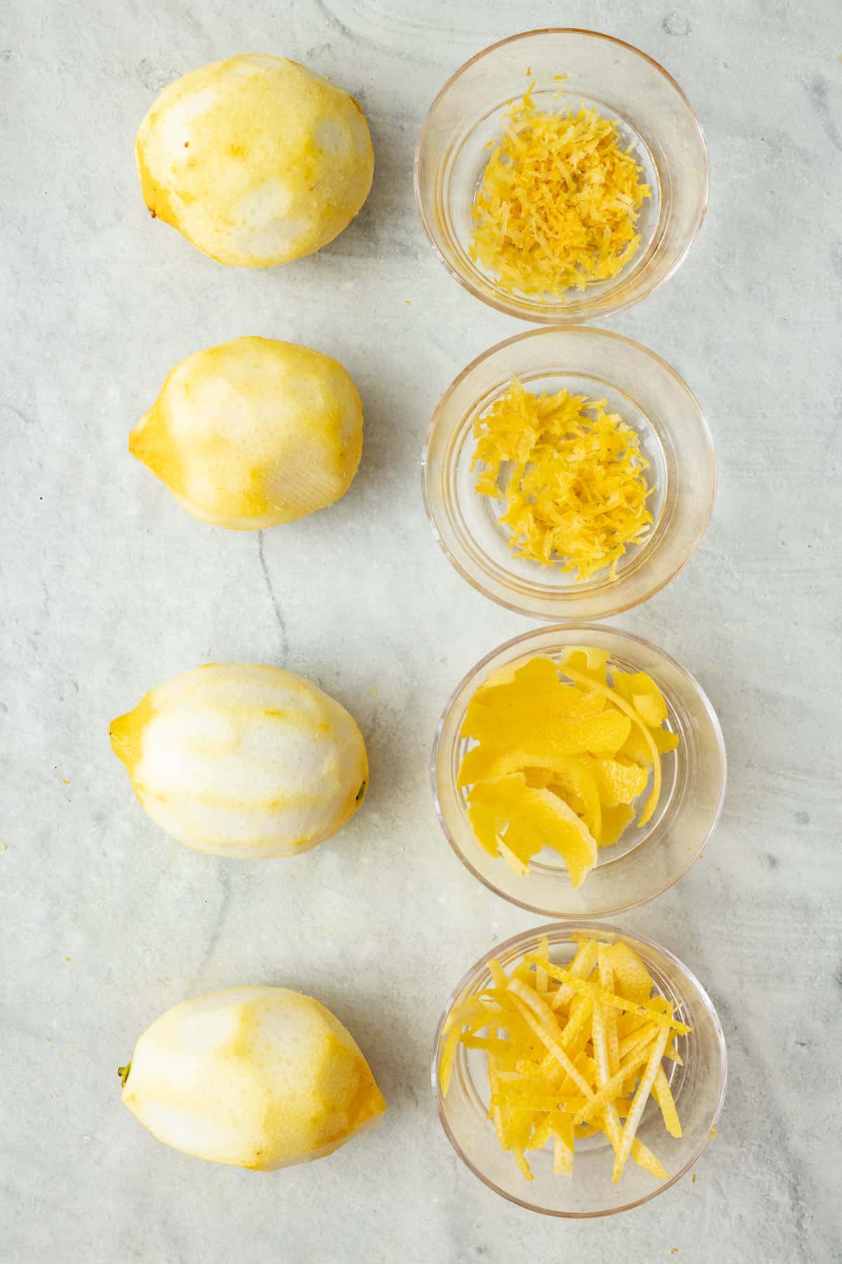 4 lemons on a cutting board after being zested, a different way for each, and the zest from each one next to it in a small bowl
