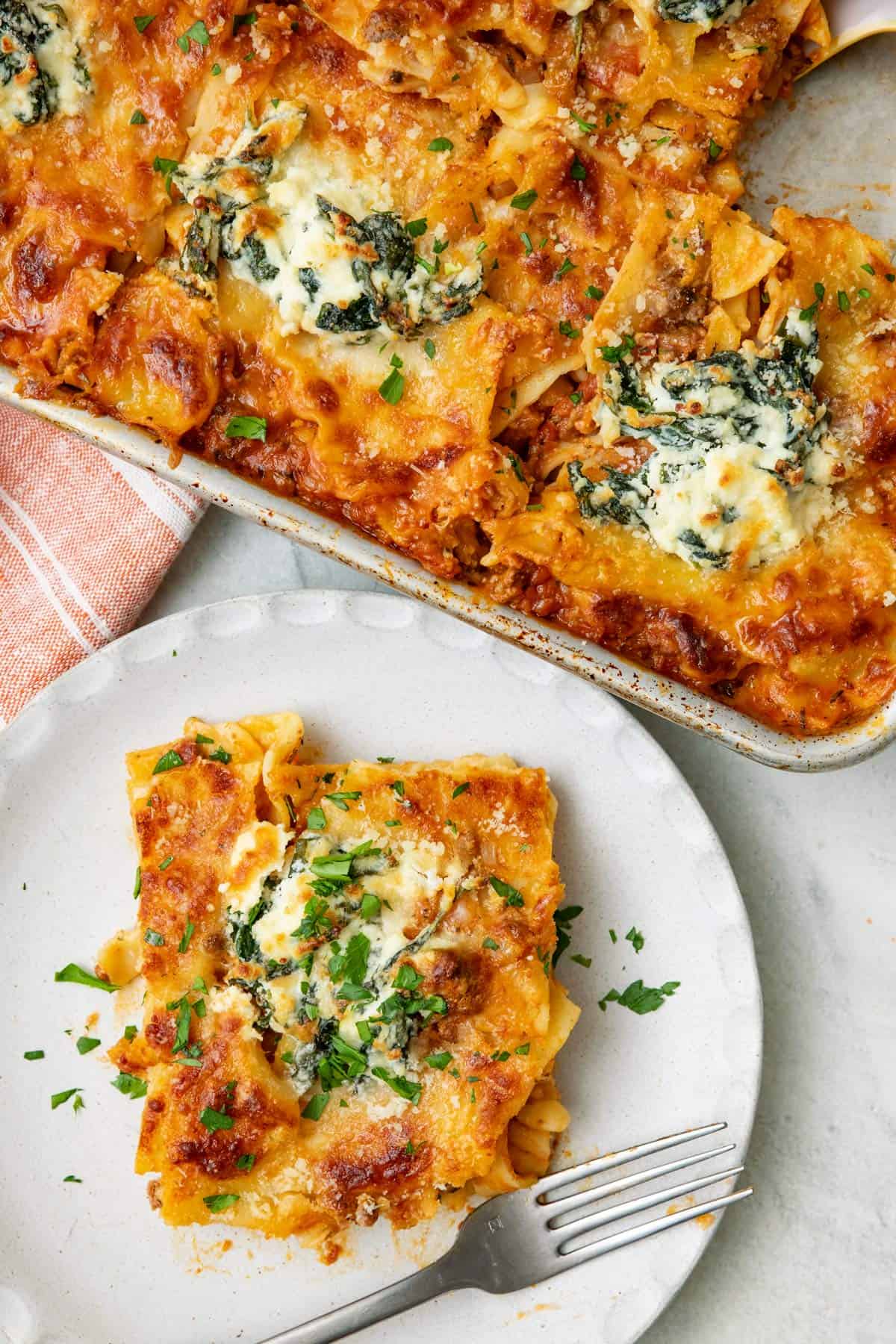 A serving of layerless lasagna on a plate with baking dish nearby.