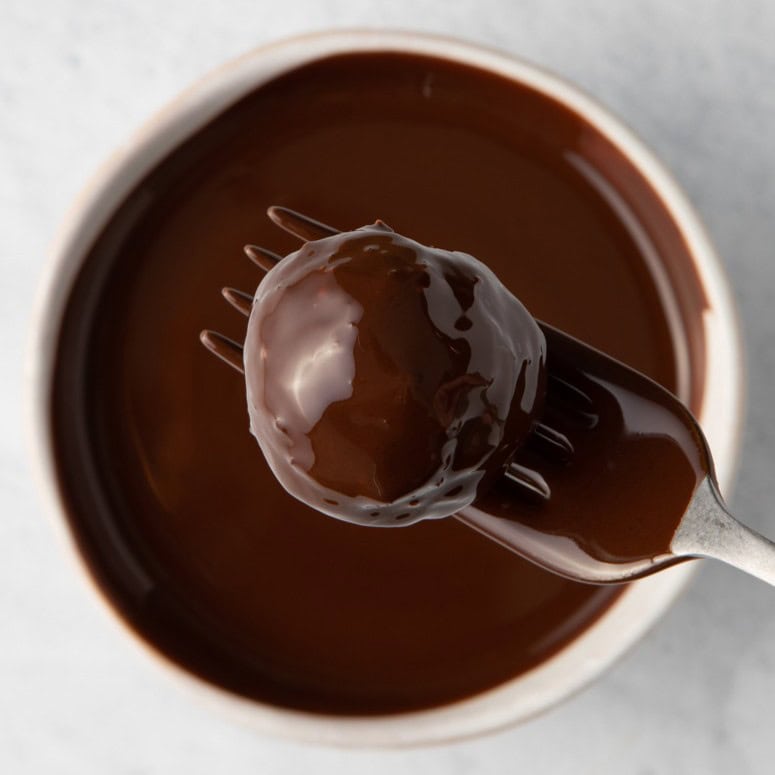 Chocolate covered coconut ball on fork on top of small bowl or melted chocolate.