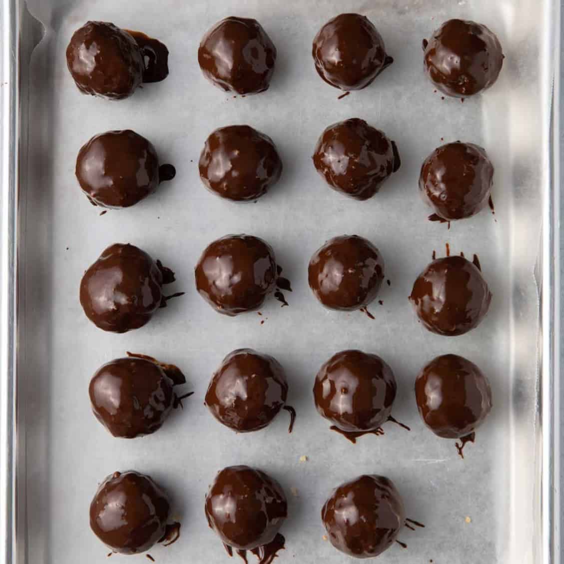Parchment lined baking sheet with coconut balls after dipped in chocolate.
