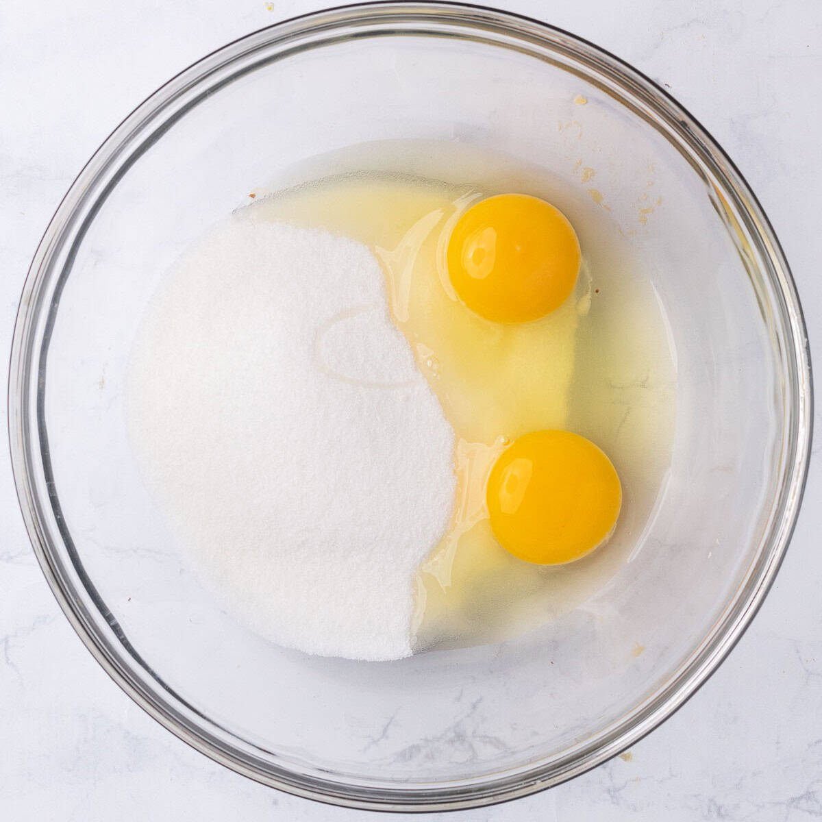 Sugar and 2 whole eggs in a bowl before mixing.