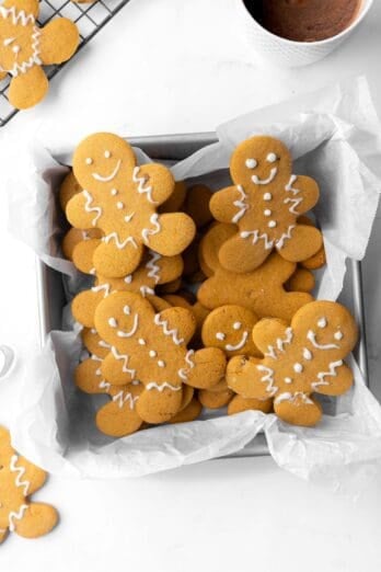 Gingerbread cookies stack in a parchment lined square tin.