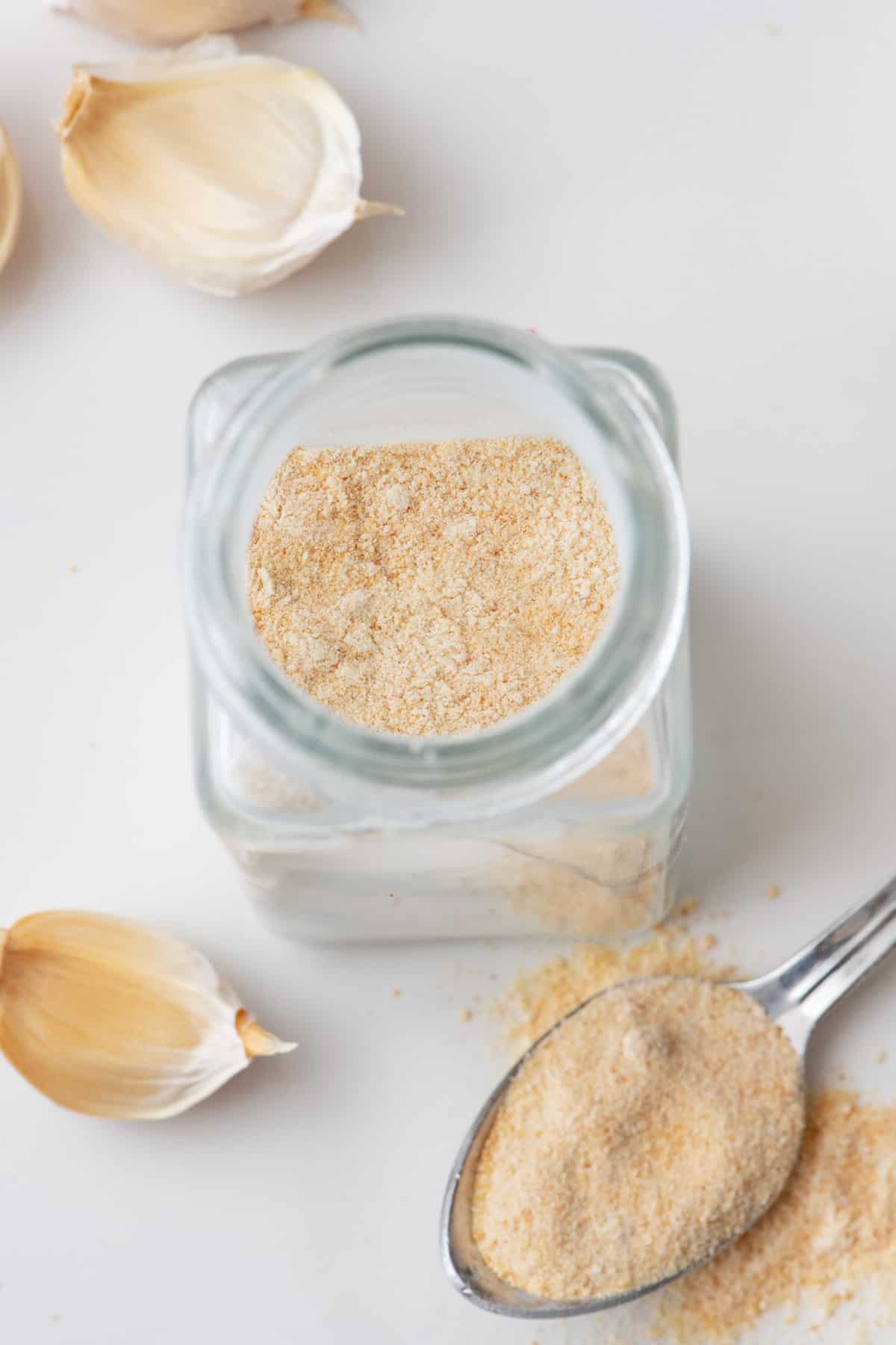 Homemade garlic powder in a spice jar with a full spoon of garlic powder nearby.