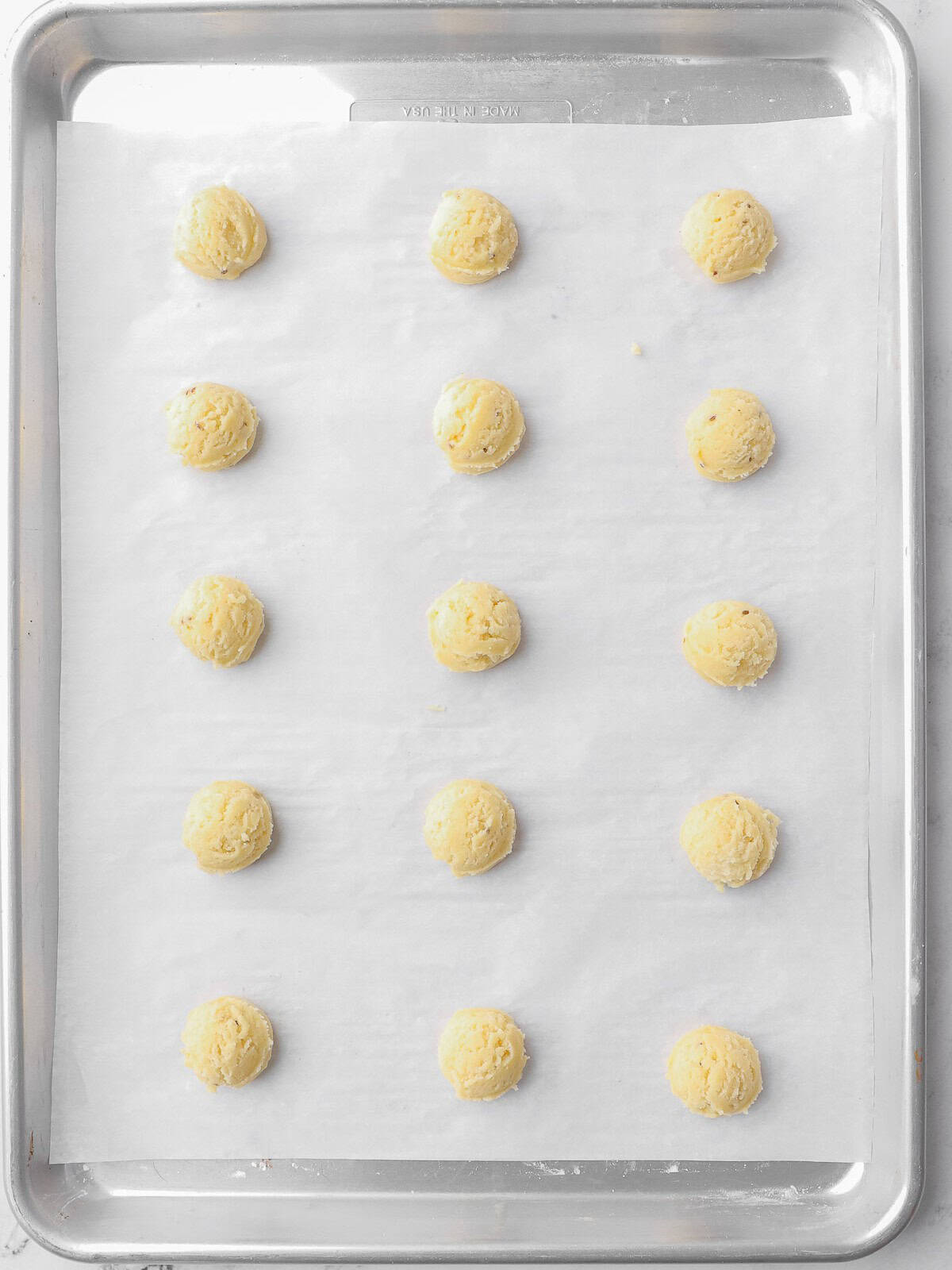 Cookie balls on a parchment line baking sheet before baking.