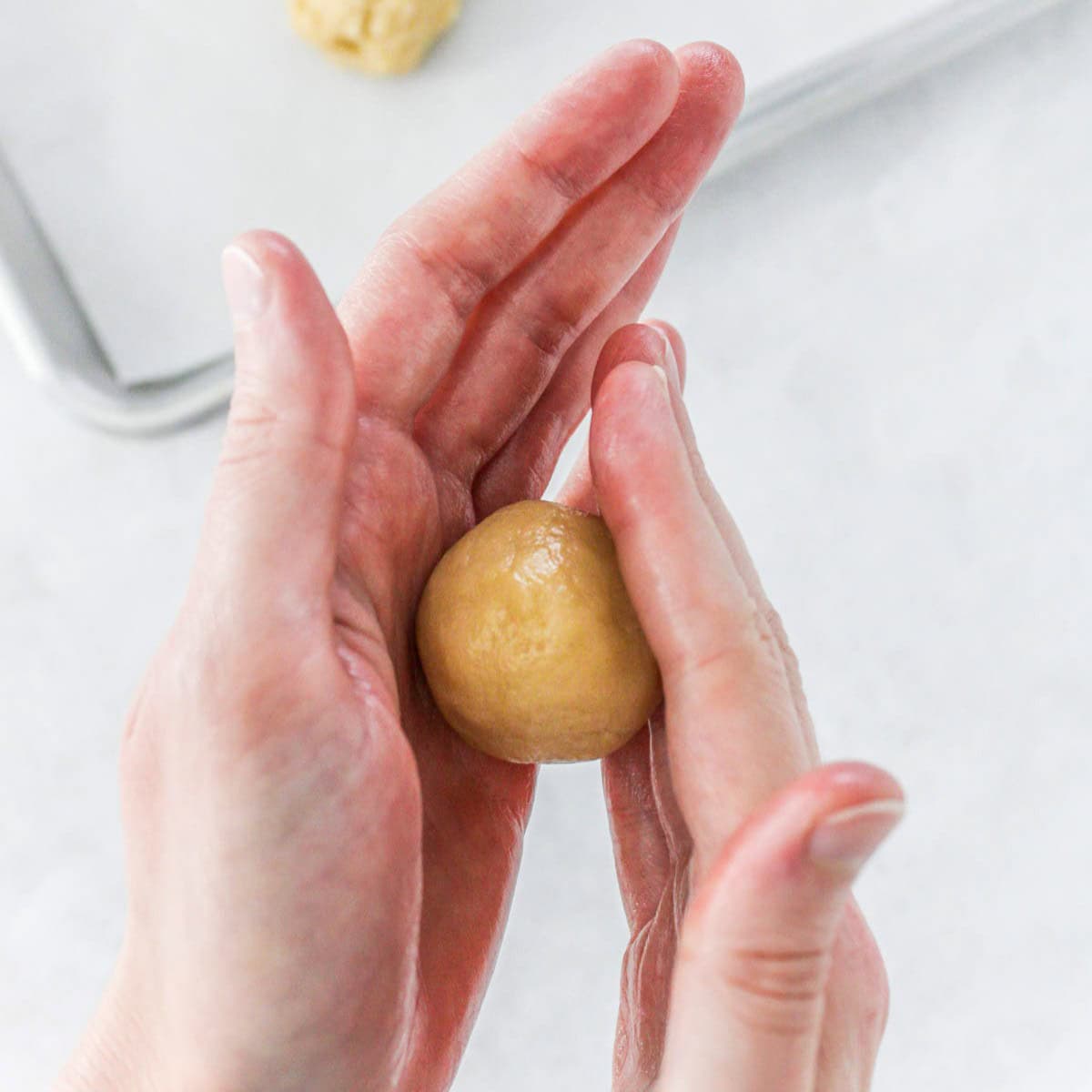 Hands rolling a scoop into a round dough ball.