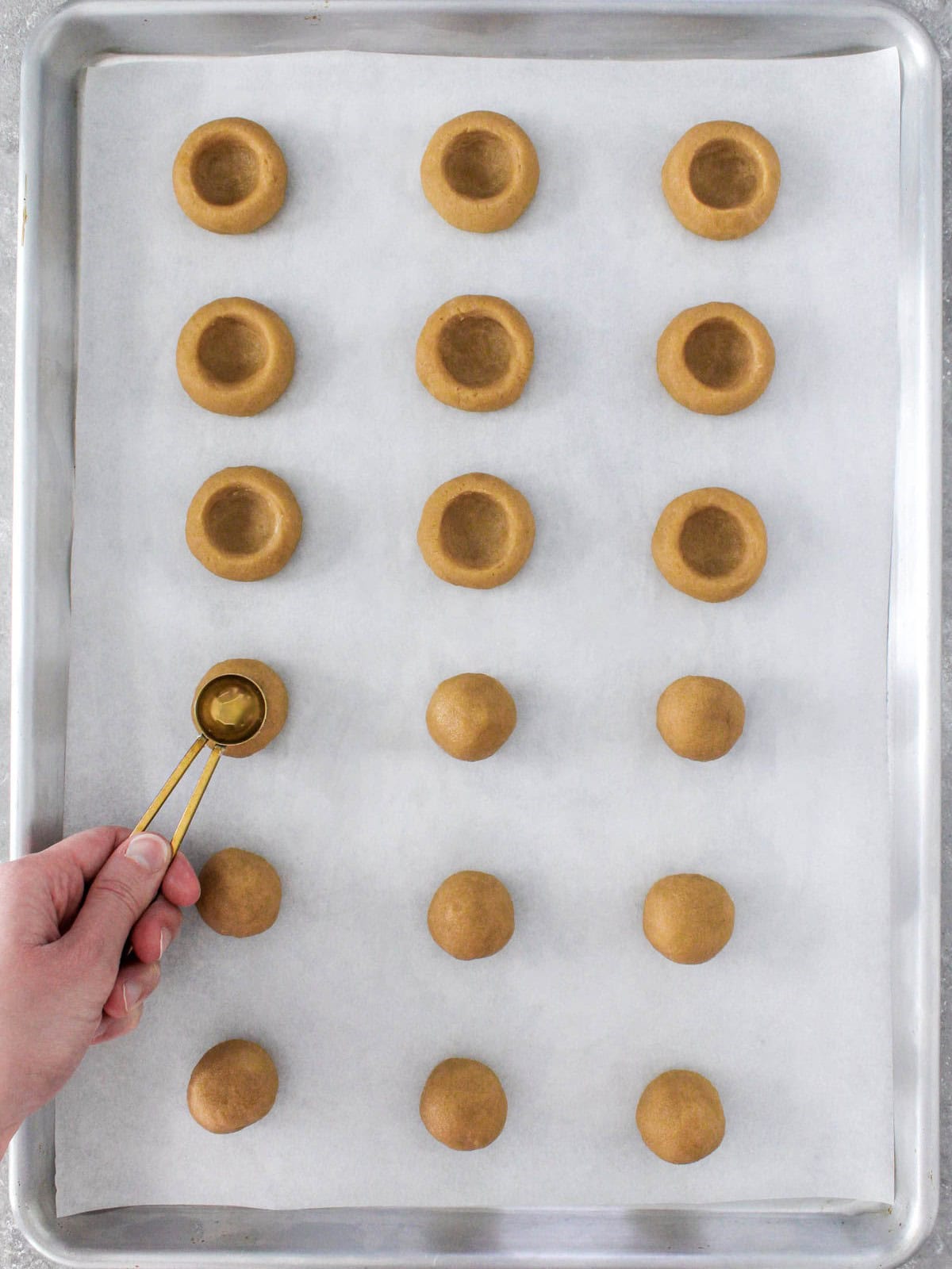 Pressing an indent into cookies with thumb or ยฝ round teaspoon with a few already prepared.