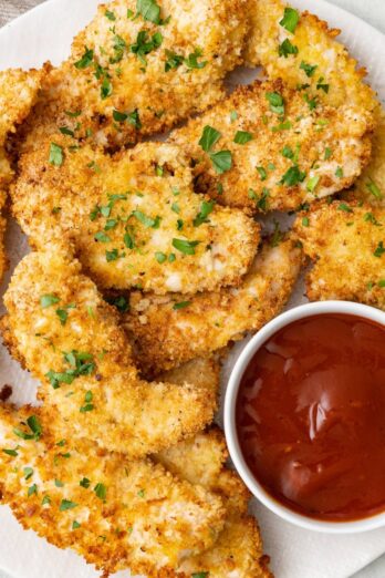 Square image of a plate of crispy air fryer chicken tenders with a small bowl of bbq sauce for dipping.